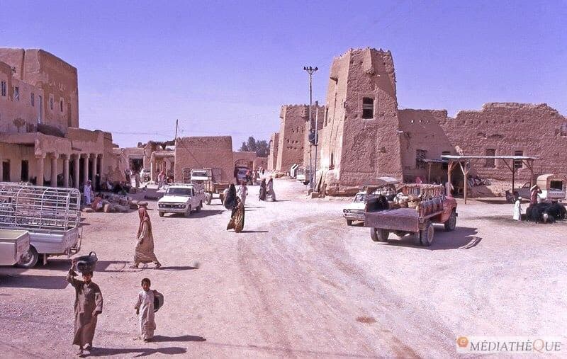 مشهد أرشيفي منشور على أنه لمدينة ليلى عام 1974م؛ تظهر فيه الأبراج والمباني الطينية وحركة الشارع.
